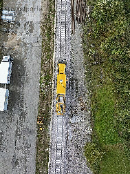 A yellow construction machine on a railway track next to a storage yard and some vehicles  tamping machine  Hermann Hessebahn  Althengstett  Black Forest  Germany  Europe