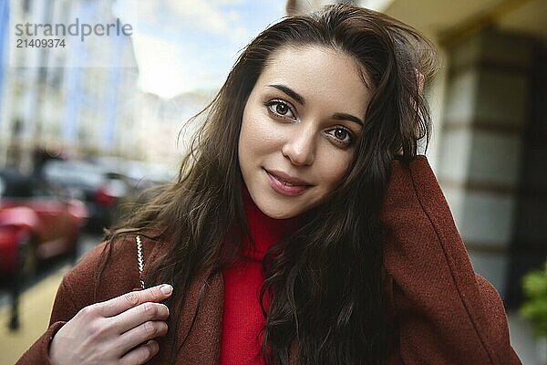 Portrait of a fashionable woman posing for the camera in a brown coat and red sweater