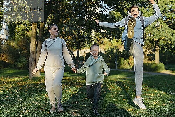 A family mom and 2 sons are having fun  running in the park and jumping. Sons  children  mom  run  play  rejoice  enjoy nature in summer. Family teamwork. Happy family team  running together in field  happily waving their hands. Group of people of different ages. happy family  mom and two sons on an emotional walk. Running and enjoying life in a green field in the park  blue sky  nature