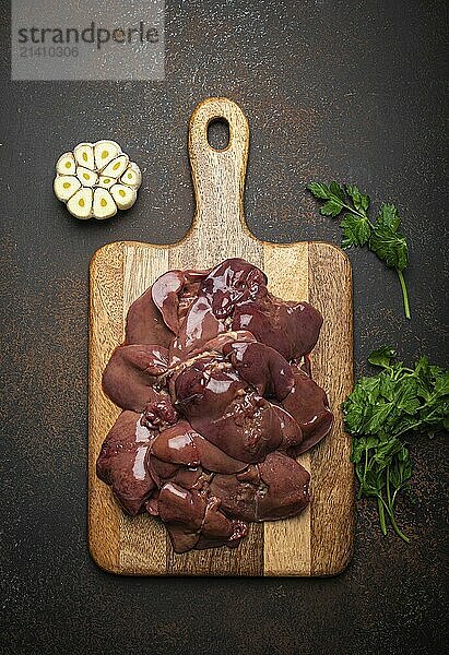 Raw chicken liver on wooden cutting board top view on dark rustic concrete background kitchen table with parsley and garlic. Healthy food ingredient  source of iron  folate  vitamins and minerals  food photography  food photography