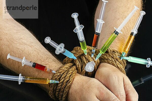 Close-up bound hands and colorful syringes stucked from it. Drug addiction and hostage concept