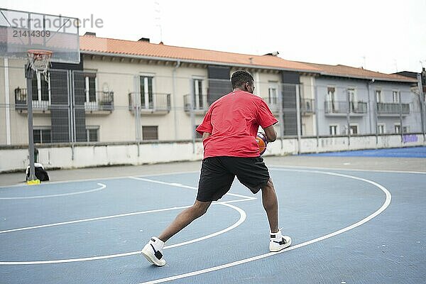 Rear view of an unrecognizable african american young man playing basketball outdoor at urban court