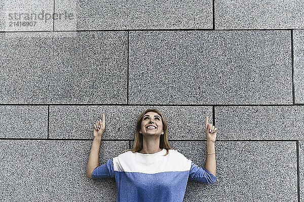 Cheerful girl at the street  show a big sale  or nice offer. Advertise concept. People  travel and tourism  woman on city street and girl show with her fingers something over gray wall background