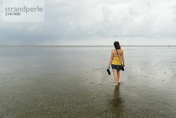 Young woman walking alone in a calm and tranquil beach at low tide in Wadden Sea  Germany. View from behind