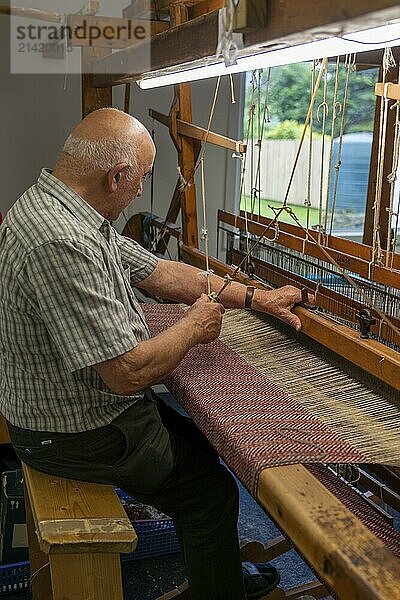 Ardara  Ireland  13 July  2022: master craftsman working on a traditional wooden loom and hand weaving woollen herringbone cloth  Europe