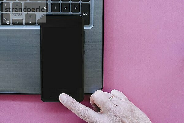 Mockup of mobile phone with blank copy space screen with laptop and woman hand on pink background. Flat lay  top view