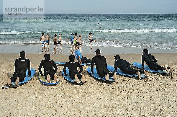 27.09.2019  Sydney  New South Wales  Australia  Young men lie on surfboards in the sand while taking part in a surfing course on Bondi Beach. Children play football in the background  Oceania