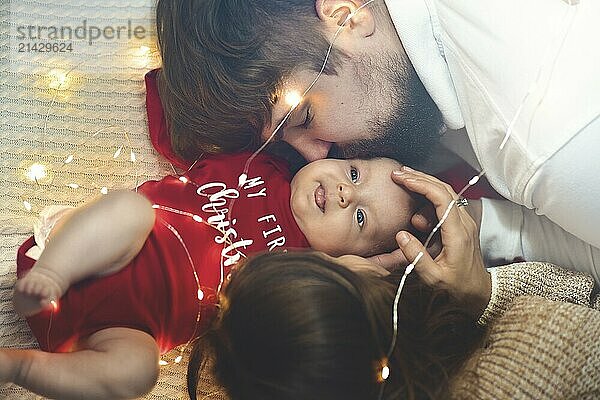 Top view. Mother and Father Kisses Baby in Bed. Little Newborn Child in White Bed. Parenthood Concepts. Love and Happiness. Taking Care of New Life