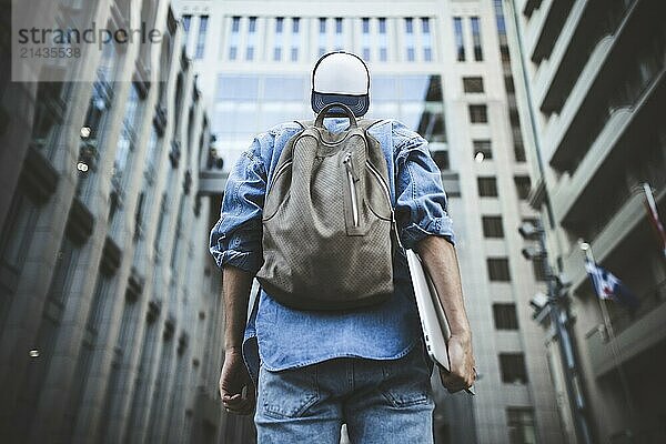 Outdoor portrait of handsome young male student with backpack standing at building background on the street while waiting his colleagues. Businessman wearing casual white shirt and spectacles. People