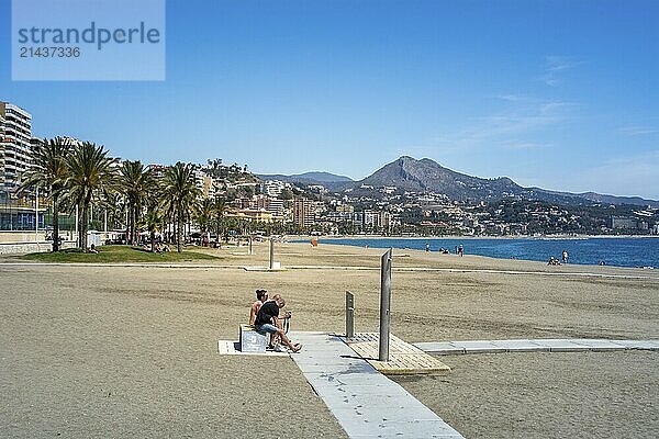 Malaga  Spain  April 2016: view on La Malagueta beach on a sunny and day with clear sky in summer. Palm trees  city architecture and mountains in the background  Europe