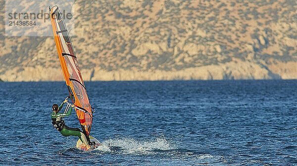 Person windsurfing at high speed over the sea in front of a mountain backdrop  windsurfer  Meltemi windsurfing spot  Devils Bay  Paralia Vatha  Vatha Beach  southeast coast  Karpathos  Dodecanese  Greek Islands  Greece  Europe