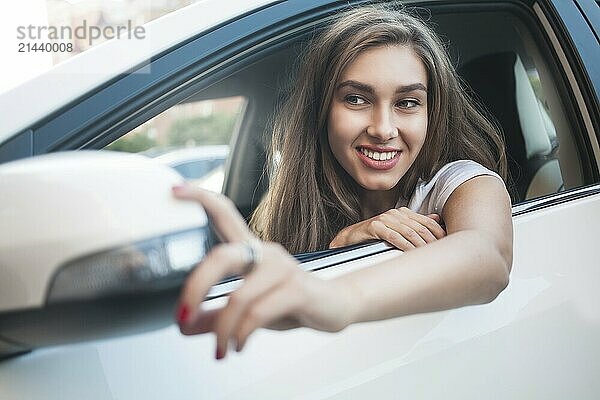 Portrait of cute smiling girl sit in the car and look at the car mirror