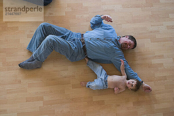 A top view of a small boy lying down on the floor with his father.