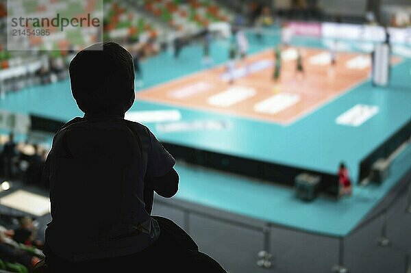 Silhouette of little boy piggyback by his father and volleyball match in the background