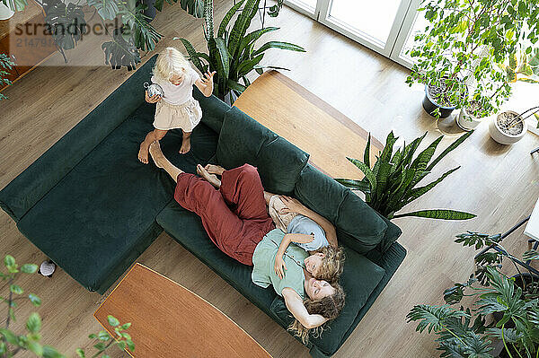 Mother resting with daughters on sofa in living room at home