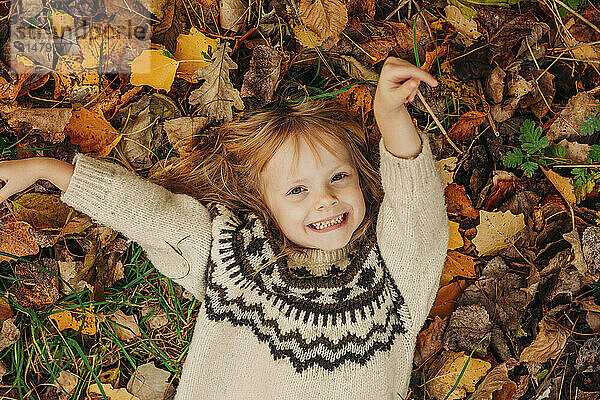 Happy girl lying on leaves in autumn park