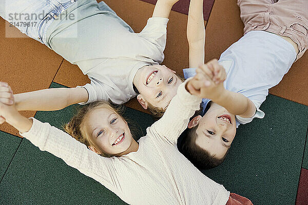 Smiling friends holding hands and lying down in school playground