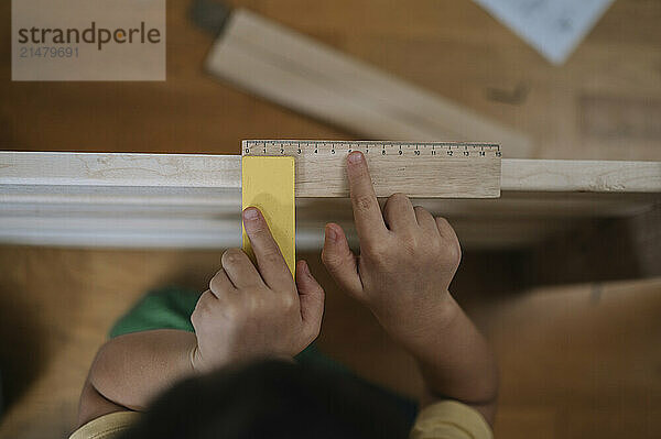 Boy measuring furniture with ruler at home