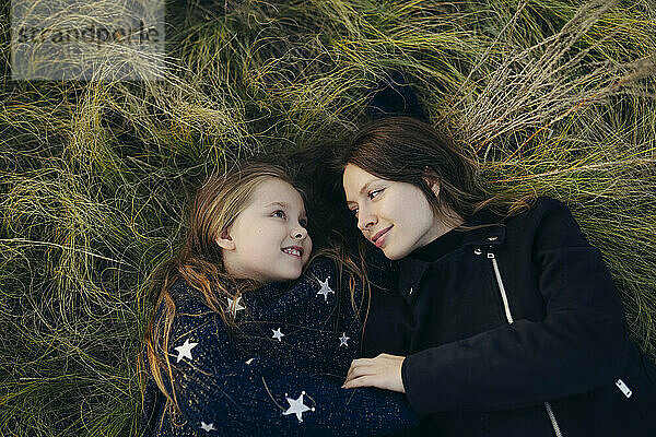 Smiling mother and daughter lying down on grass