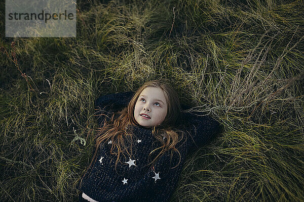 Girl with hands behind head lying down on grass