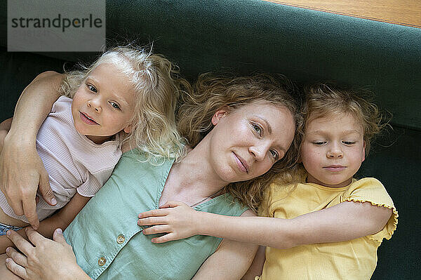 Smiling woman lying with daughters on sofa at home