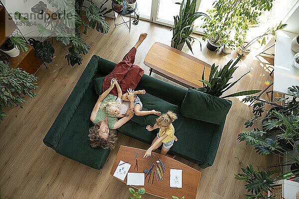 Girl drawing with mother and sister lying on sofa at home