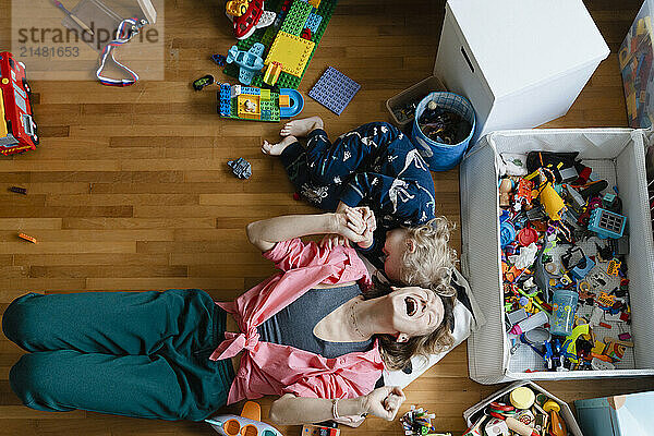 Mother and son laughing together amidst toys in bedroom at home