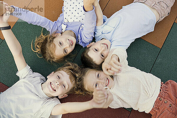 Happy kids holding hands and lying down at school playground