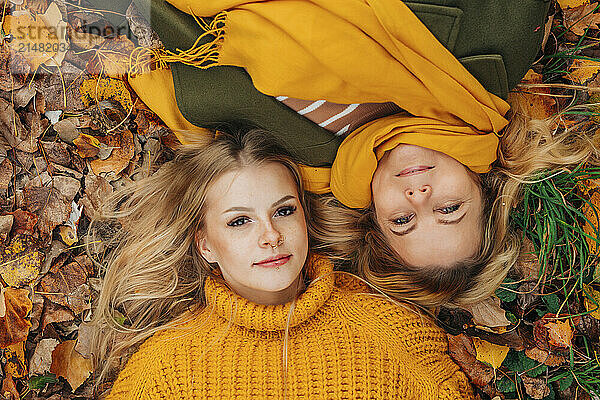 Smiling mother and daughter lying on autumn leaves in park