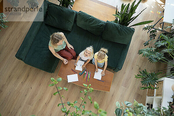 Happy girl drawing with mother and sister in living room at home