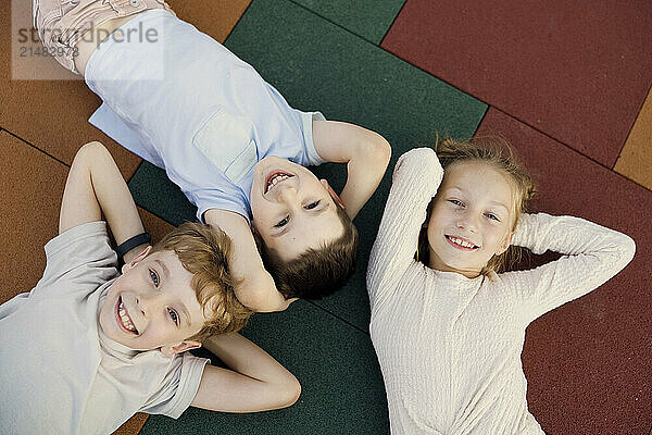 Happy kids lying down with hands behind head at school playground