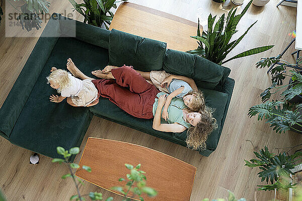 Mother resting with daughters on sofa at home