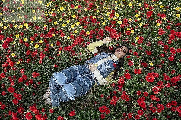 Young happy girl resting in the field of red poppy flowers. Drone aerial of woman in spring