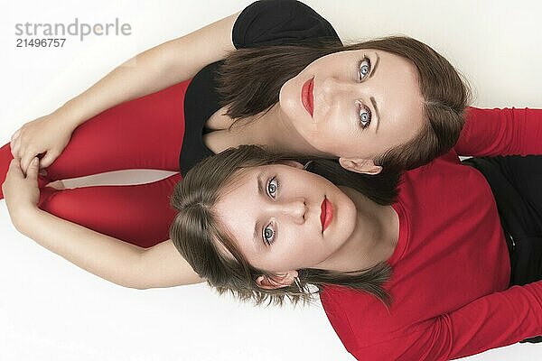 Top view of mom and daughter sitting with their backs to each other and put their heads on each other's shoulders. Both women looking up at camera. Studio shot  part of photo series