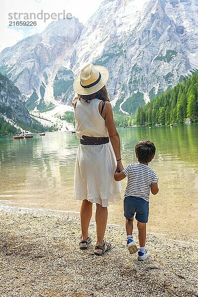 Mother and son admiring stunning panorama of lake braies  surrounded by majestic mountains and lush greenery in italian dolomites