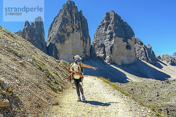 Woman carrying child hiking and pointing at the landscape near tre cime di lavaredo  dolomites  a famous landmark of the italian alps