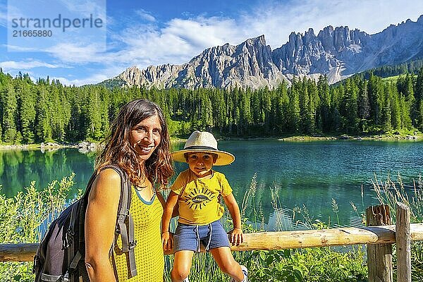 Mother and son enjoying the stunning scenery of lake carezza with the latemar mountain range in the background  dolomites  italy