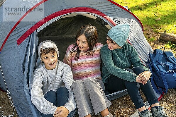 High angle view of three smiling brothers sitting on camping tent enjoying nature