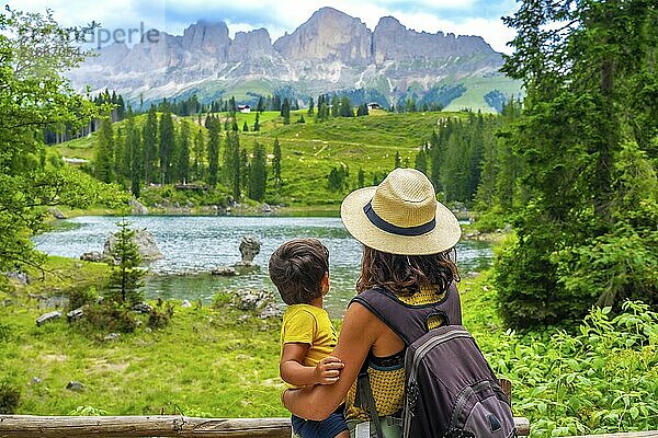 Mother carrying her son while enjoying breathtaking views of emerald waters at lake carezza  surrounded by the dolomites