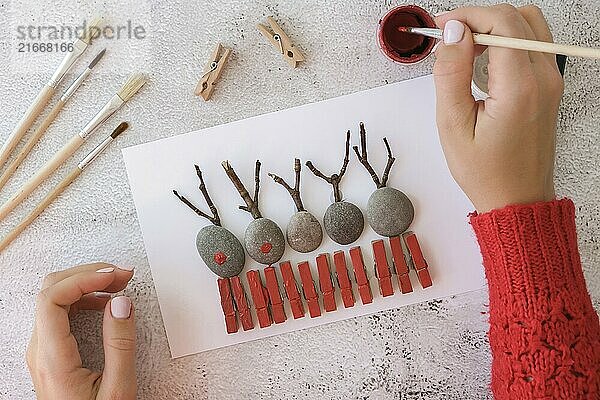 Step by step. Top view. Process kid children craft. Do it yourself Diy Merry Christmas deer on greeting card postcard made of pebbles  sea stones  clothespins and branches on white background. Natural Eco style diy. Gift idea