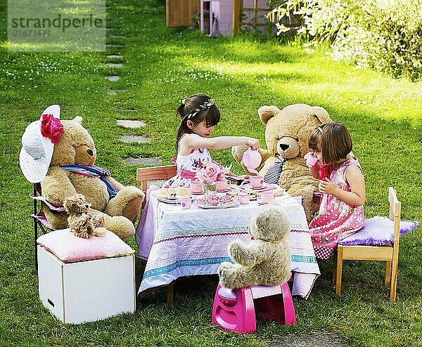 Elevated view of two young girls playing Teddy Bears Picnic in their back garden themes of imagination daydreaming playing