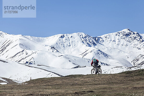 Cyclist riding on a mountain trail with snow-covered peaks in the background under a clear blue sky. Concept of adventure and outdoor activity