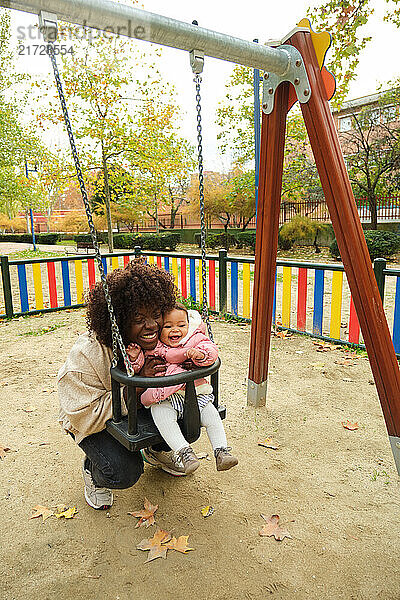 Happy mother and baby daughter having fun on a swing in a colorful playground