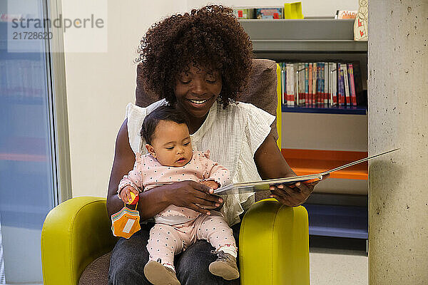 Young mother reading a book to her baby daughter  enjoying quality time together in a comfortable library setting