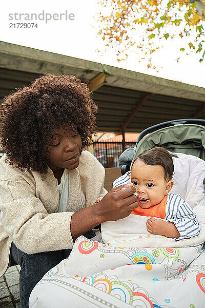 Loving mother feeding her baby while sitting in a stroller  enjoying a meal outdoors