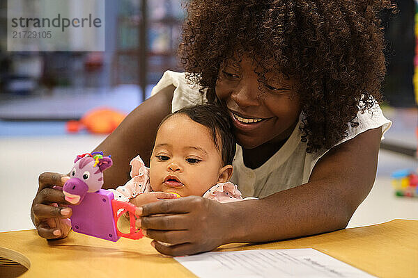 Smiling mother and baby girl playing together with an educational toy at a daycare center  promoting early childhood development