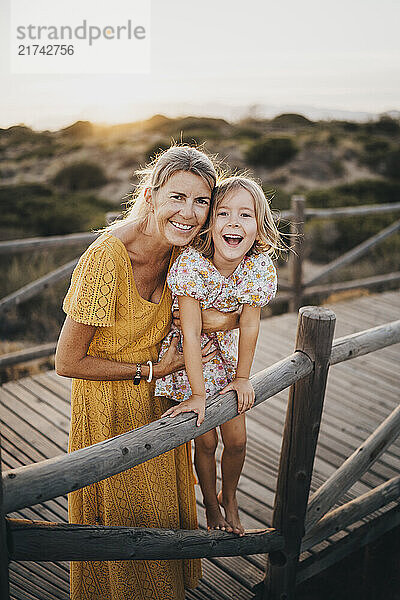 Mother and daughter hugging laughing at beach on summer sunset