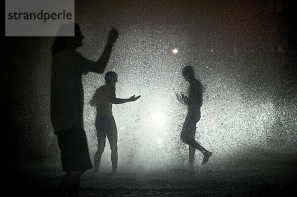 Illuminated by police lights  people revel in a the sudden downpour produced by broken fire hydrant in Venice Beach  Los Angeles  Calif.  on July 4  2011. The hydrant was run over by a car  sending a geyser three stories into the air. Authorities eventually cleared the area and shut off the water supply.