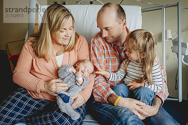 Family on hospital bed with newborn baby after birth mom dad sister