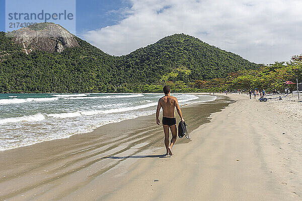 Beautiful tropical beach landscape with man walking  green water  lush forest and blue sky in Ilha Grande  Costa Verde  south Rio de Janeiro  Brazil